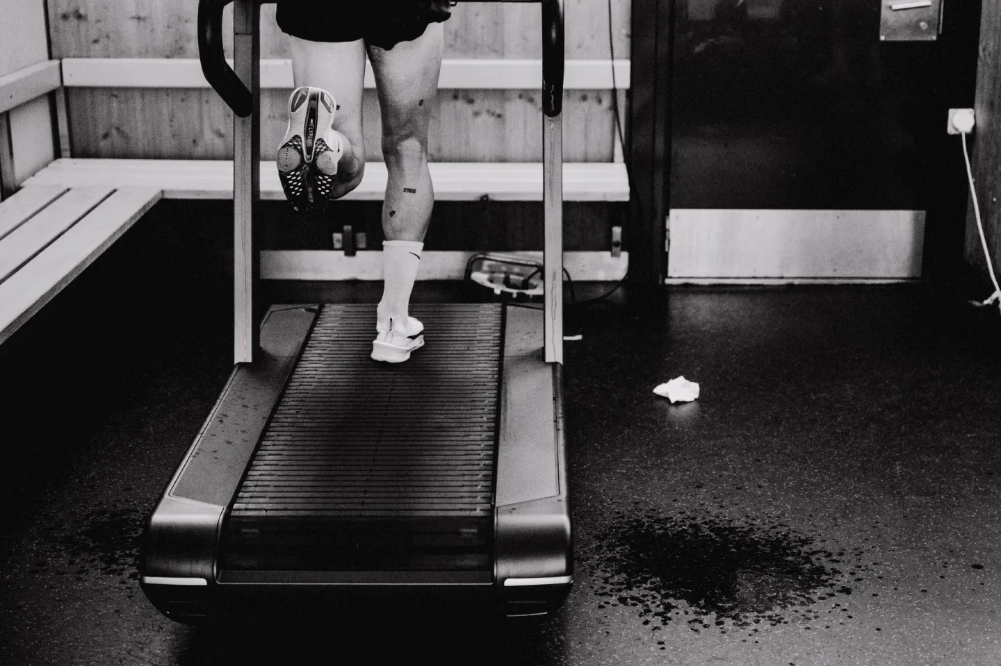Runner from behind on a curved treadmill, sweat on the floor